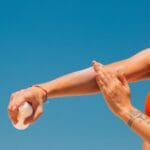 Kobieta na plaży nakłada krem z filtrem na skórę pod błękitnym niebem