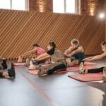 Ranking sportów poprawiających postawę ciała które aktywności naprawdę pomagają na garbienie i bóle pleców Dorośli rozciągający się na matach w nowoczesnej siłowni dla zdrowej postawy